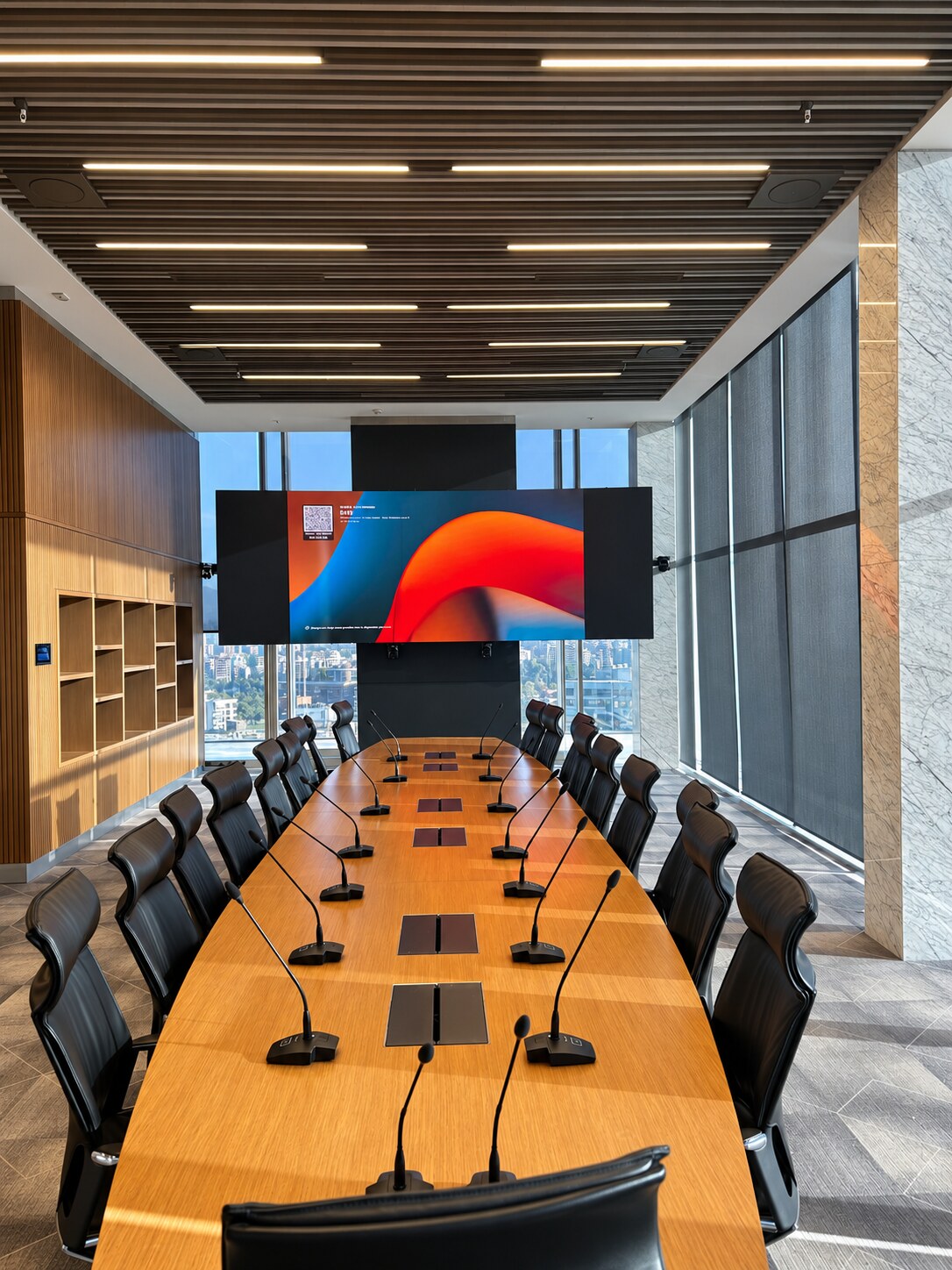 Sala de directorio con mesa larga, micrófonos individuales y pantallas para reuniones.