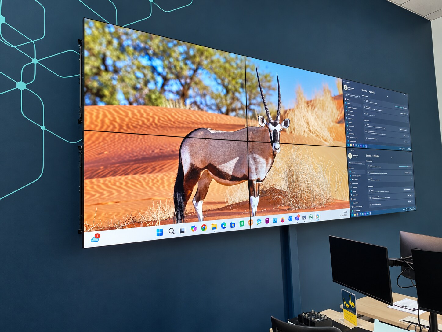 Videowall formado por varias pantallas, instalado sobre una pared junto a puestos con monitores.