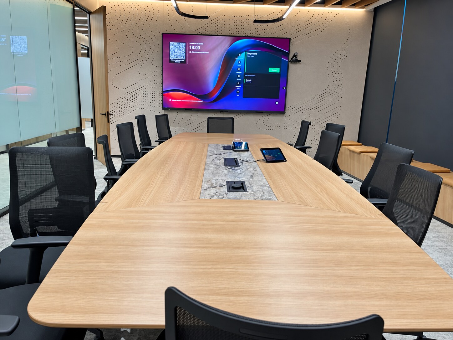 Sala de reuniones con pantalla mural, cámara y dispositivos de control integrados en la mesa.